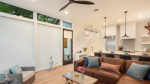A modern living room with a brown leather sofa, a glass coffee table, and a ceiling fan.