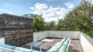 A rooftop patio with a wooden deck, a white sofa with light blue cushions, and a small table.