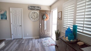 A hallway with a wooden floor, a welcome sign, a clock, and a door. - Prinstine 4BR Havasu Home — Tons of Boat Parking & Dual AC (Lake Havasu City)