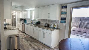 A kitchen with white cabinets, a stainless steel trash can, a countertop with a coffee maker, toaster, and a small table. - Prinstine 4BR Havasu Home — Tons of Boat Parking & Dual AC (Lake Havasu City)