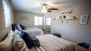 A bedroom with two beds, a ceiling fan, a shelf with decorative items, and a window with blinds. - Prinstine 4BR Havasu Home — Tons of Boat Parking & Dual AC (Lake Havasu City)