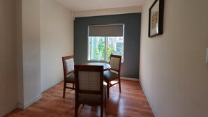 A dining area with a table and chairs, a window with a view of greenery, and a framed picture on the wall.