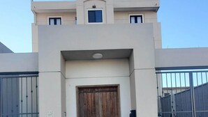 A modern building with a central wooden door, two metal gates on either side, and a small window above the door.