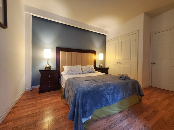 A bedroom with a bed, two bedside tables with lamps, a wardrobe, and a wooden floor.