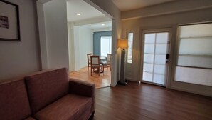 A living room with a brown sofa, wooden flooring, a dining area with chairs and a table, and a lamp.