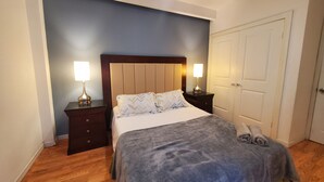 A bedroom with a bed, two bedside tables with lamps, a wooden headboard, a door, and a wooden floor.