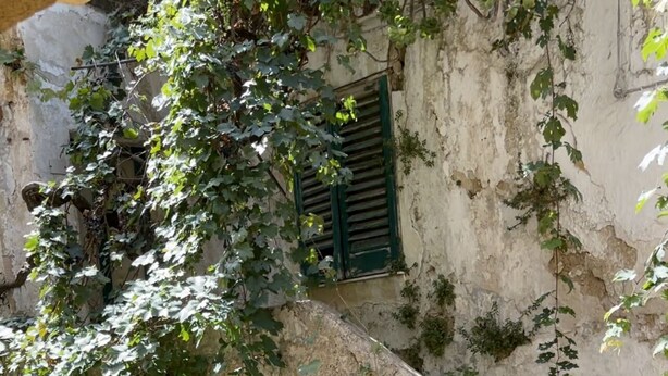 Un estrecho callejón con una rústica pared de piedra, una puerta de madera y una barandilla de metal.