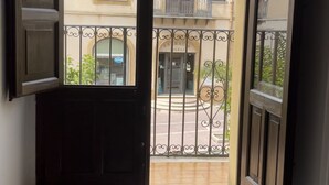 Vista desde un balcón con barandilla de metal, un edificio con varias ventanas y una puerta que da a la calle.