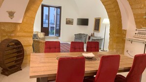 Un comedor con una mesa de madera y sillas rojas, una pared de piedra con arco, un sofá y un televisor.