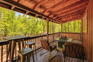 Um deck de madeira com uma mesa e cadeiras, com vista para uma floresta.
