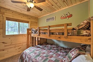 Quarto estilo cabana com paredes de madeira e beliche. Uma placa na parede diz 'Aventura Espera'.