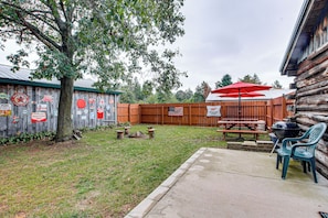 Un patio trasero con cerca de madera, mesas de picnic y zona de parrilla.