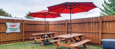Un patio trasero con cerca de madera, mesas de picnic y sombrillas rojas.