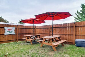 A backyard with a wooden fence, picnic tables, and red umbrellas. - Arkdale Studio Cabin w/ On-Site ATV Trails! (Arkdale)