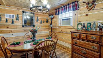 Un intérieur en bois avec une table à manger dressée pour quatre personnes, entourée de chaises, d’un lustre et d’un buffet en bois doté de tiroirs.