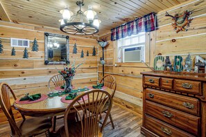 A wooden interior with a dining table set for four, surrounded by chairs, a chandelier, and a wooden cabinet with drawers.