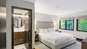 Een moderne slaapkamer met een groot bed, een inloopkast en uitzicht op bomen door de ramen.