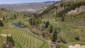 Een golfbaan met een vijver, omringd door beboste heuvels en bergen.
