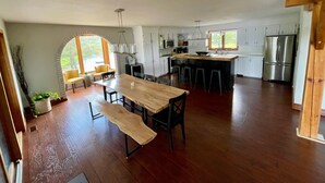 A spacious kitchen with wooden flooring, a central island with stools, white cabinets, and a large window providing natural light. - Need a summer getaway? Book NorthFork Lakehouse-the ultimate cottage destination (Sebright)