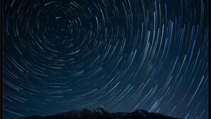Fotografía de estelas de estrellas con la silueta de una montaña en la parte inferior.