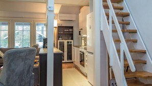 Een moderne keuken met een centraal eiland, een zithoek met een grijze stoel en een houten trap.