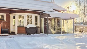 Een houten huis met een overdekte veranda en een glazen uitbouw.