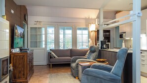 Een moderne woonkamer met een bank, fauteuils, een televisie en een keuken met een magnetron.