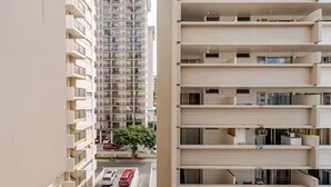 Un immeuble résidentiel à plusieurs étages, doté de balcons, avec un espace de stationnement où sont garées des voitures, et un arbre au premier plan.