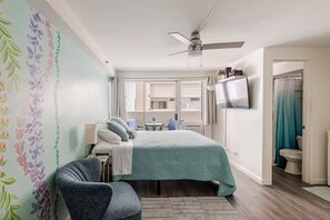 A bedroom with a bed, a chair, a TV, and a ceiling fan.