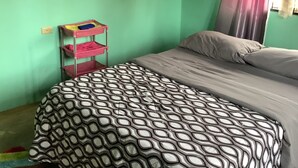A room with a bed, a bedside table, a colorful rug, and a window with curtains.