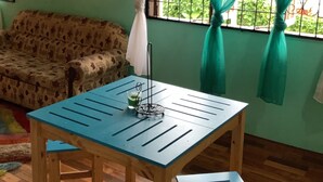 A room with a wooden table and chairs, a sofa, a clock on the wall, and a window with curtains.