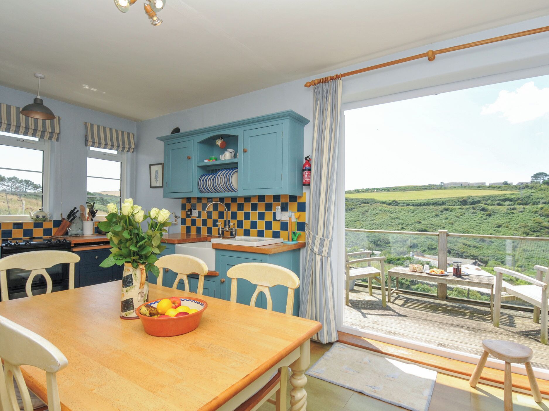 Una cocina con vistas a un paisaje verde, una mesa de comedor con sillas y un balcón con mobiliario exterior.