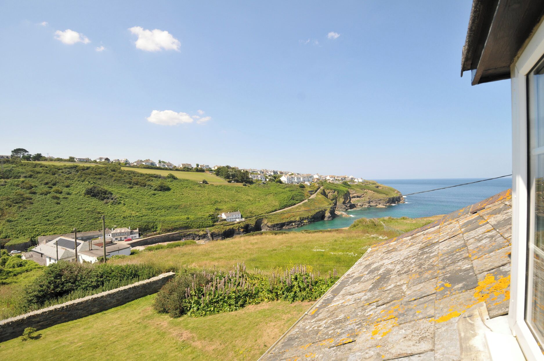 A coastal landscape with a stone wall, grassy areas, and houses in the distance.