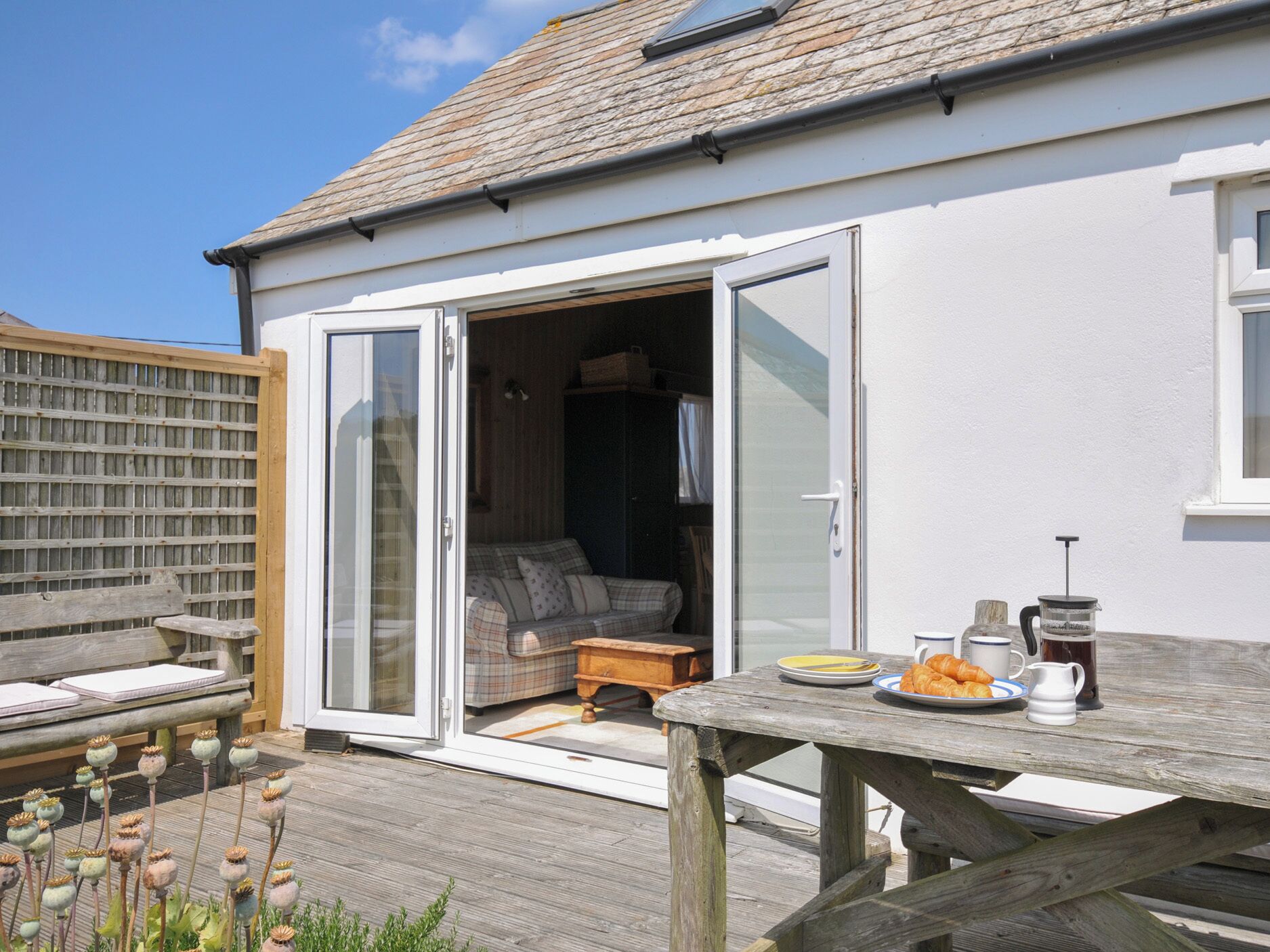A wooden deck with a table set for breakfast, a sofa, and a sliding glass door leading to an interior space.