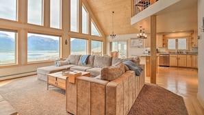 Ein geräumiges Wohnzimmer mit einem großen Ecksofa, Holzboden und großen Fenstern mit Blick auf die Berge.