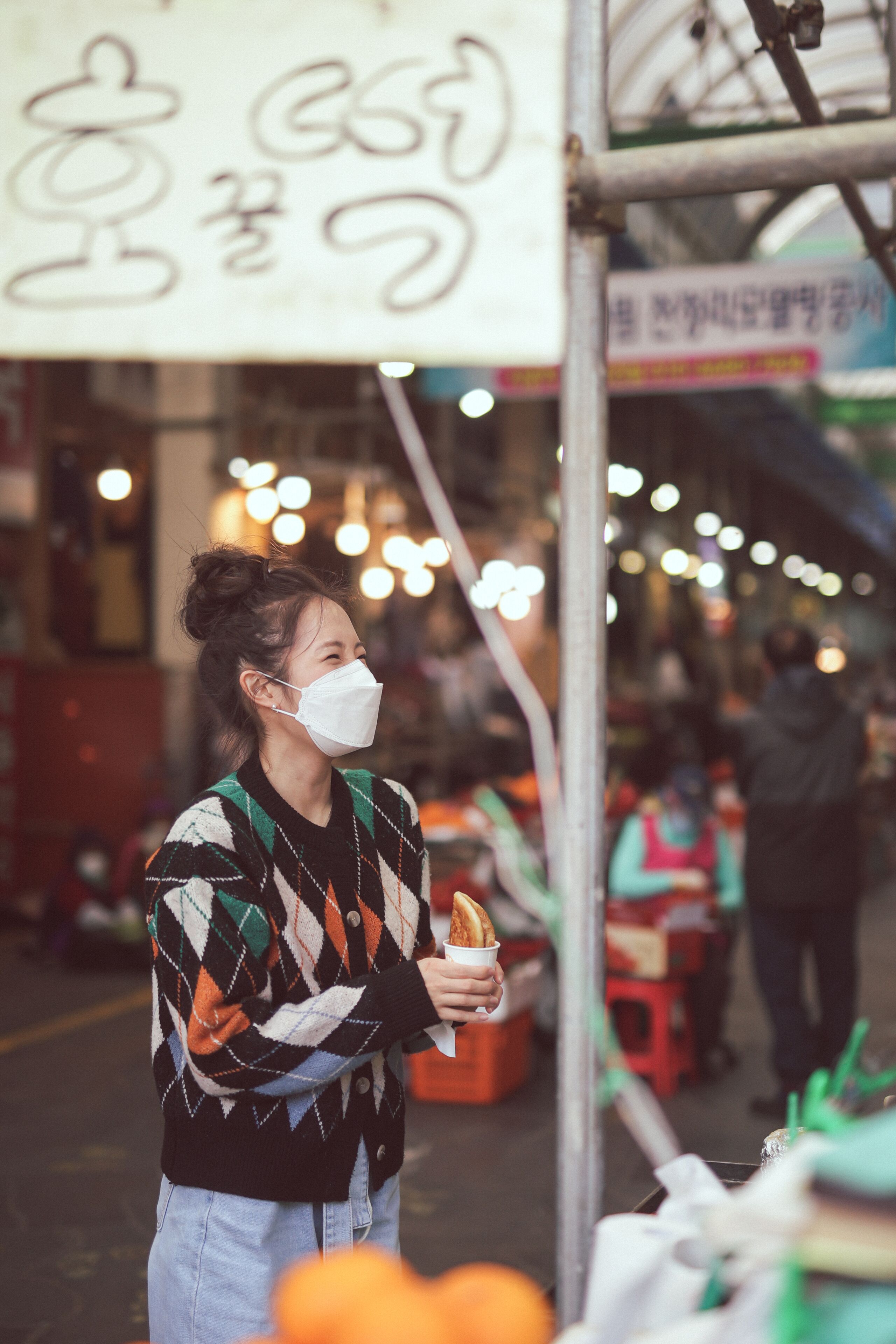 A person holding a baguette at a market stall with a sign above.