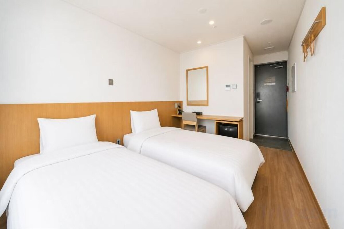 A hotel room with two beds, a desk, and a mirror.