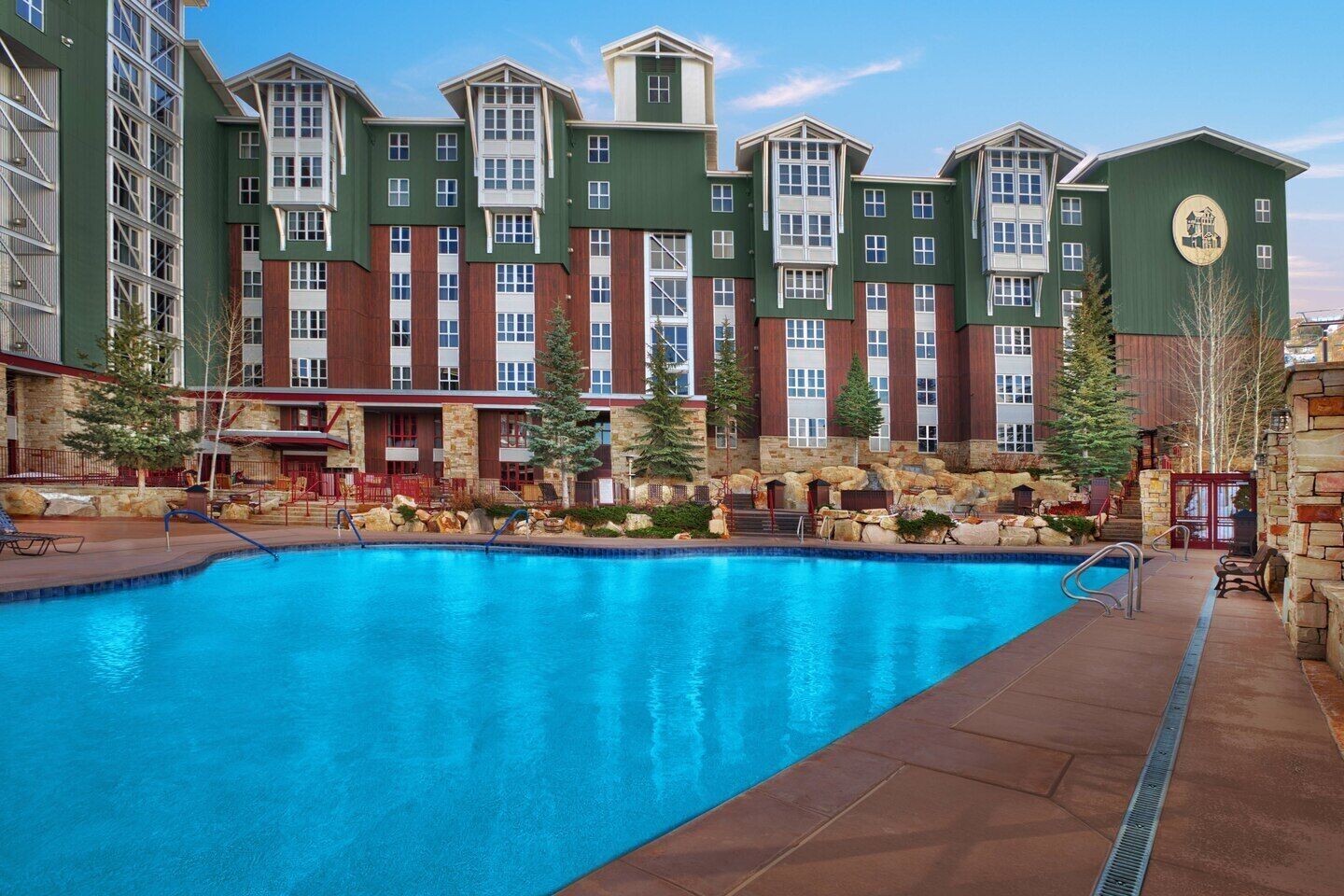 A hotel with a large outdoor swimming pool, stone walls, and a mix of modern and traditional architecture.