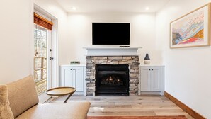 Una sala de estar con chimenea de piedra, un televisor de pantalla plana encima, un sofá y un mueble con un florero.