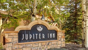 A stone sign with "JUPITER INN" written on it, surrounded by trees and greenery.