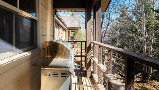 Un espacio al aire libre cubierto con una parrilla, cubierta de madera y vistas a una casa y árboles.