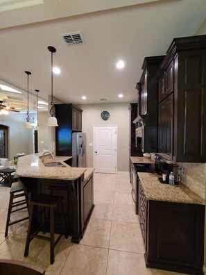 A modern kitchen with granite countertops, dark wooden cabinets, and pendant lighting. - Isabella's getaway (Edinburg)