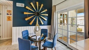 A dining area with a round table, blue chairs, and a large wall clock.