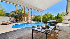 A covered outdoor area with a pool, patio furniture, and a barbecue grill.