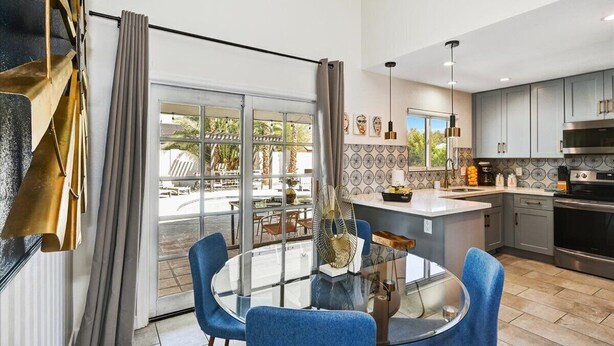 A modern kitchen with a central island, a dining area with a glass table, and a view of the outdoors.