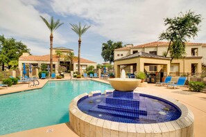 Relax by the resort pool, surrounded by lounge chairs and umbrellas, with a hot tub at its center.