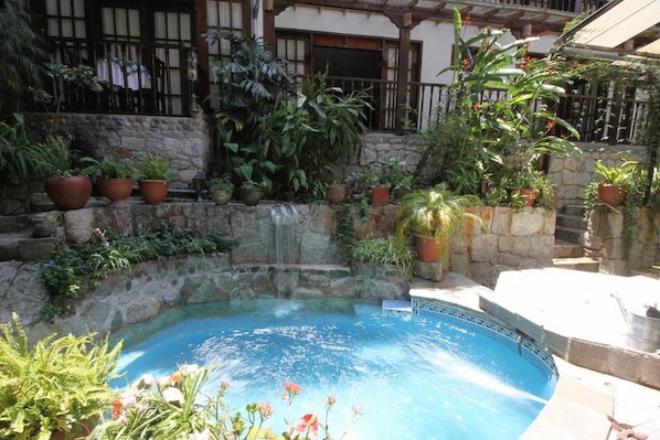 A swimming pool surrounded by stone walls and potted plants.