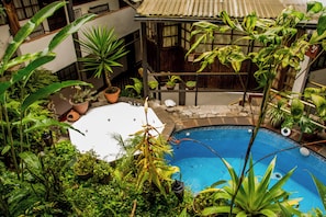 A rooftop pool surrounded by lush tropical plants, with a hot tub and a staircase leading to an upper level.