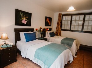Een hotelkamer met twee bedden, een nachtkastje met een lamp, een vaas met bloemen en kunstwerken aan de wanden.