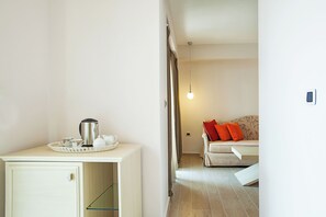 A modern hotel room with a kitchenette, a sofa with red cushions, and a hanging light fixture. - Core Hotel (Kassandra)